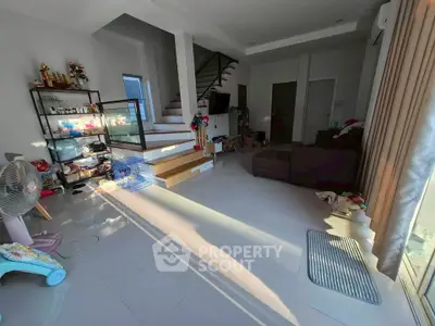 Spacious living room with modern decor and natural light, featuring a staircase and cozy seating area.