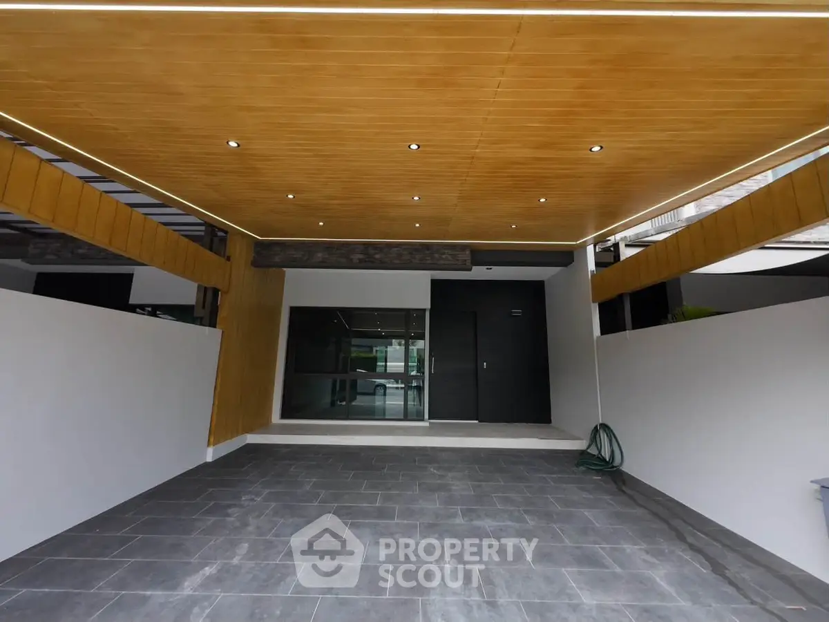 Modern home entrance with sleek wooden ceiling and spacious driveway.