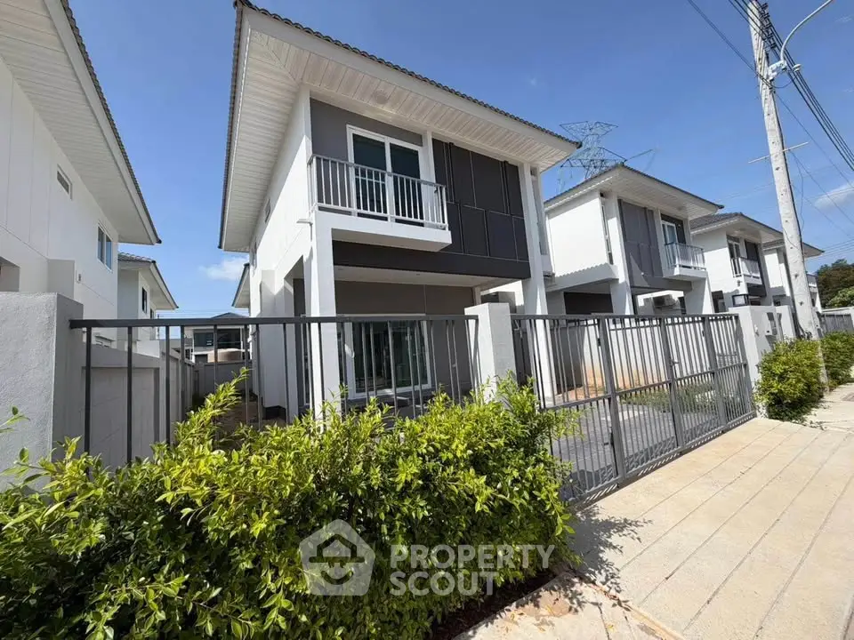 Modern two-story house with balcony and gated entrance in a serene neighborhood.