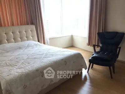 Spacious bedroom with large window and stylish chair, offering natural light and comfort.