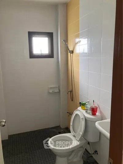 Compact bathroom with shower and toilet, featuring tiled walls and a small window for natural light.