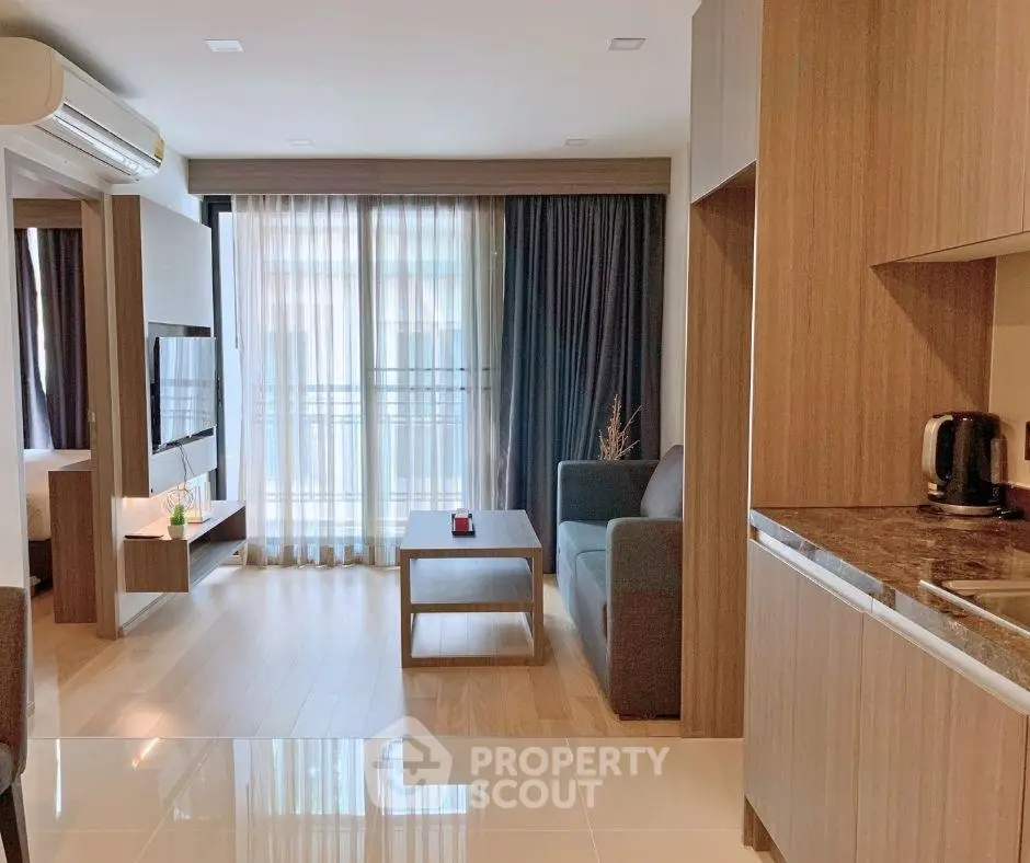 Modern open-plan living room with sleek kitchen and cozy seating area, featuring large windows and stylish decor.
