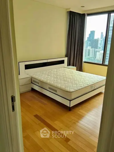 Spacious bedroom with city view and modern furnishings in high-rise apartment.