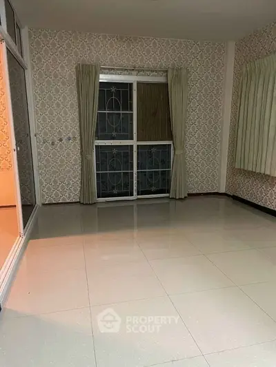Spacious empty room with tiled floor and patterned wallpaper, featuring large windows with curtains.
