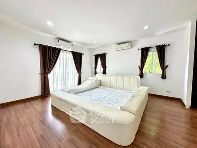 Spacious bedroom with elegant wooden flooring and luxurious white leather bed