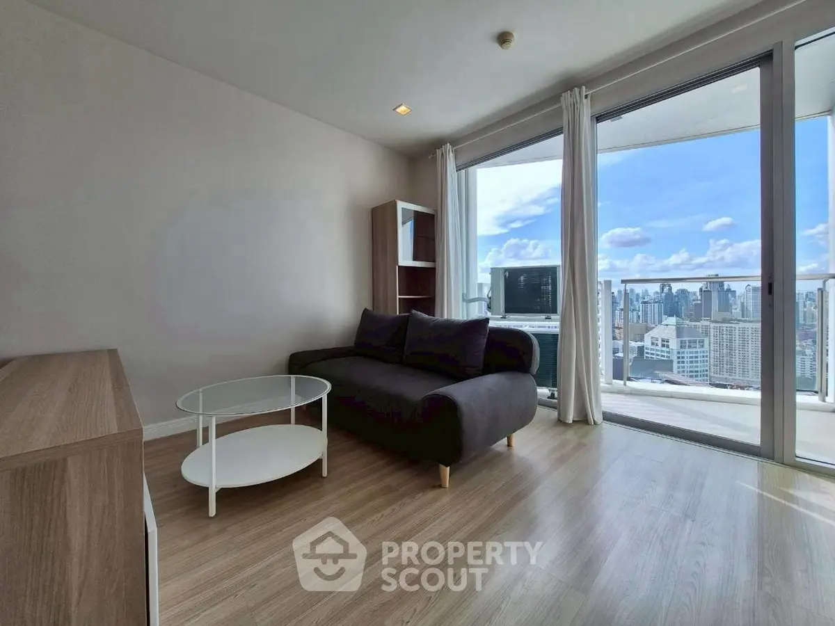 Modern living room with city view, featuring sleek furniture and large windows opening to a balcony.
