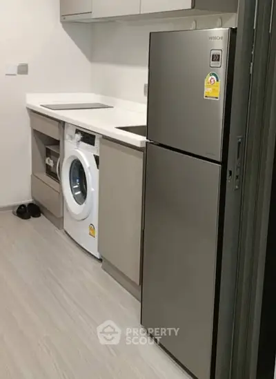 Modern kitchen with sleek appliances including fridge and washing machine in compact layout.