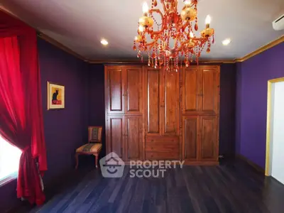 Elegant bedroom with rich purple walls, wooden wardrobe, and ornate chandelier