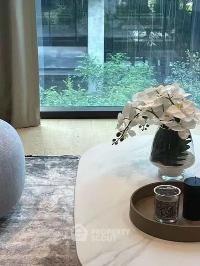 Elegant living room with large window and stylish decor, featuring a marble table and floral arrangement.