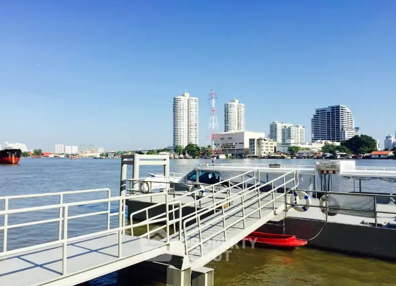 Scenic riverside view with modern high-rise buildings and clear blue sky.