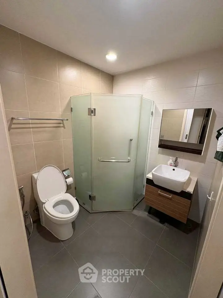 Modern bathroom with glass shower, sleek sink, and neutral tiles.