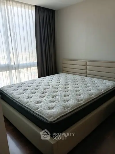 Cozy bedroom with large window and modern bed frame, perfect for relaxation.