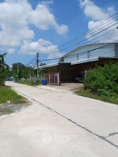 Spacious industrial warehouse with large driveway and lush greenery, perfect for business operations.