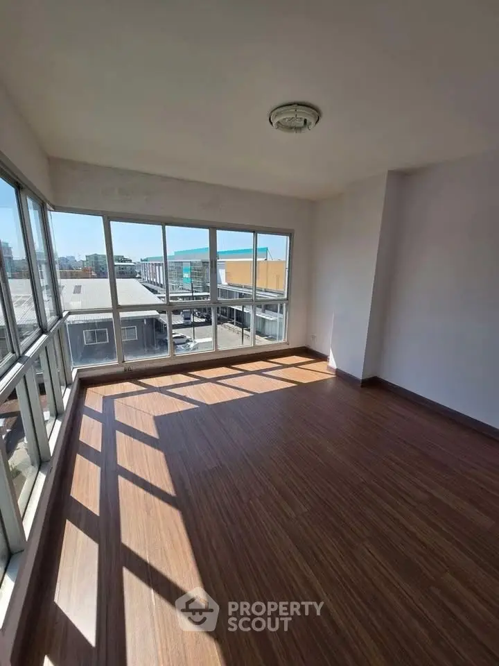 Spacious sunlit room with large windows and wooden flooring, ideal for modern living.