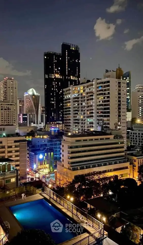 Stunning cityscape view with illuminated skyscrapers and a rooftop pool at night.