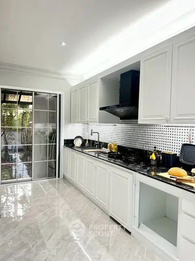 Modern kitchen with sleek white cabinetry and black countertops, featuring a gas stove and open layout.