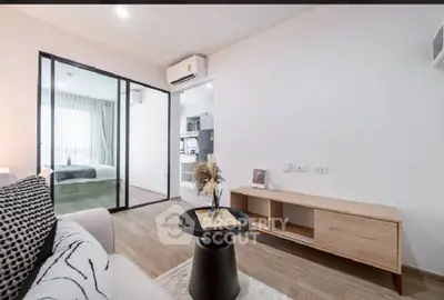 Modern living room with open layout and view into bedroom, featuring sleek furniture and natural light.