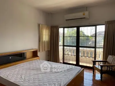 Spacious bedroom with large windows and balcony access, featuring wooden flooring and air conditioning.