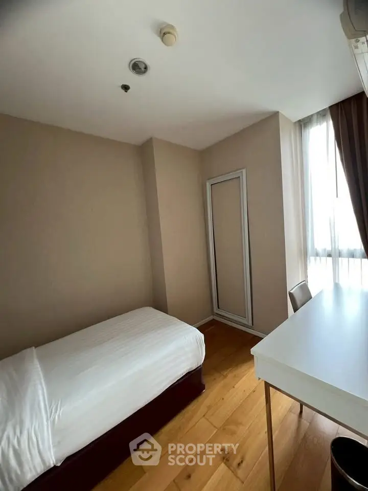 Cozy bedroom with single bed, wooden flooring, and natural light from large window.