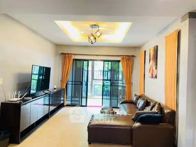 Spacious living room with modern decor and large windows leading to a balcony, perfect for relaxation.