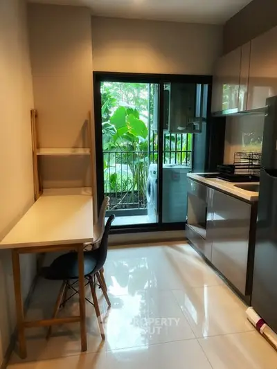 Modern kitchen with sleek cabinetry and balcony view, featuring a compact dining area and lush greenery outside.