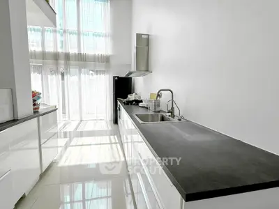 Modern kitchen with sleek countertops and high ceilings, featuring large windows for natural light.