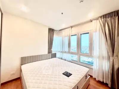 Bright and airy bedroom with large windows offering stunning city views, featuring a comfortable bed and elegant curtains.