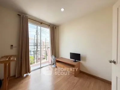 Bright living room with balcony access and wooden flooring, featuring a small TV and minimalist decor.