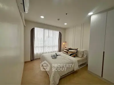 Modern bedroom with cozy bed, stylish decor, and ample natural light from large window.