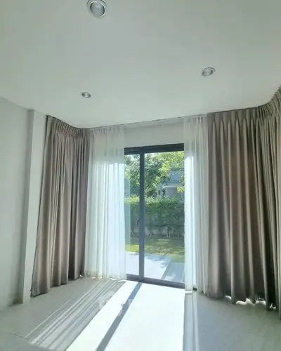 Bright room with large window and elegant curtains overlooking garden view.