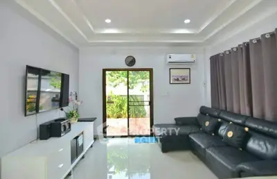 Modern living room with sleek black leather sofa and large TV, featuring elegant decor and natural light.