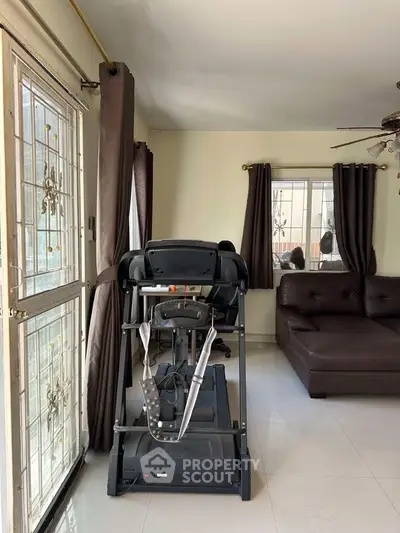 Spacious living room with treadmill and modern sofa, natural light from large windows.