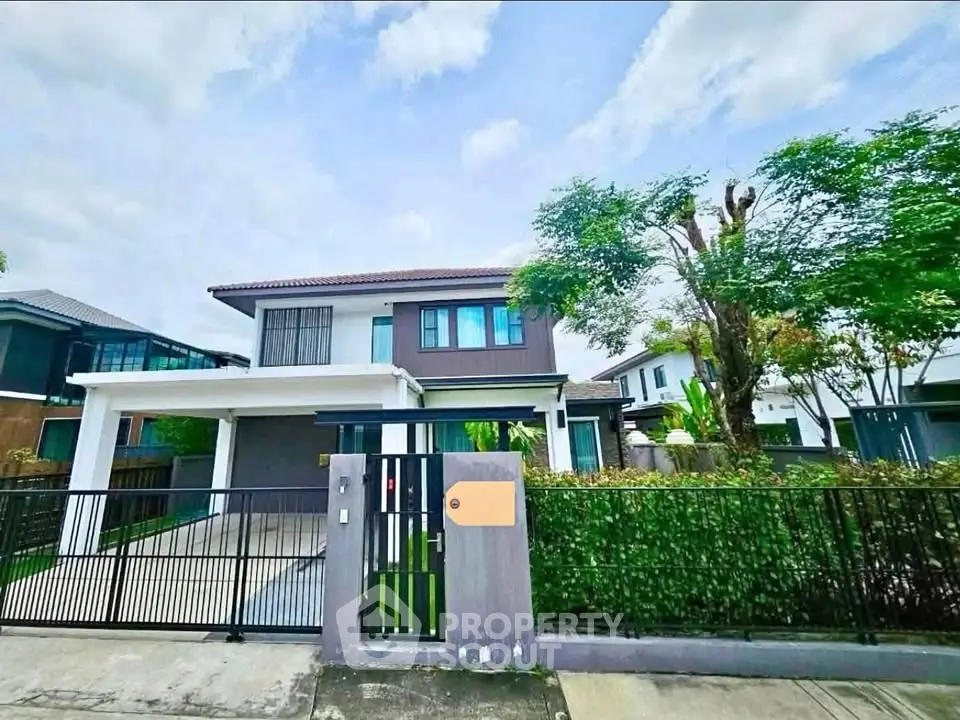 Modern two-story house with gated driveway and lush greenery in a suburban neighborhood.