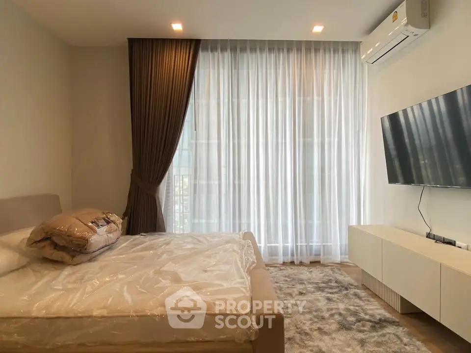 Modern bedroom with large window, stylish curtains, and wall-mounted TV for a cozy living experience.