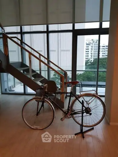Modern duplex apartment with large windows and stylish staircase, featuring a bicycle as decor.