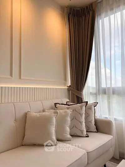 Elegant living room with plush sofa and large window with curtains, offering a cozy and bright ambiance.