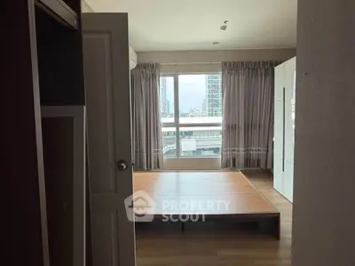 Spacious bedroom with large window and wooden flooring in modern apartment.