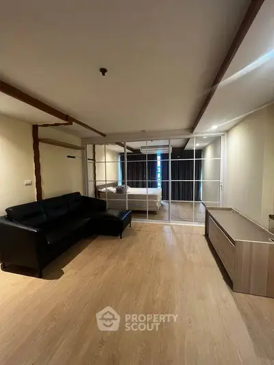 Spacious living room with modern decor and wooden flooring, featuring a cozy black sofa and elegant partition.