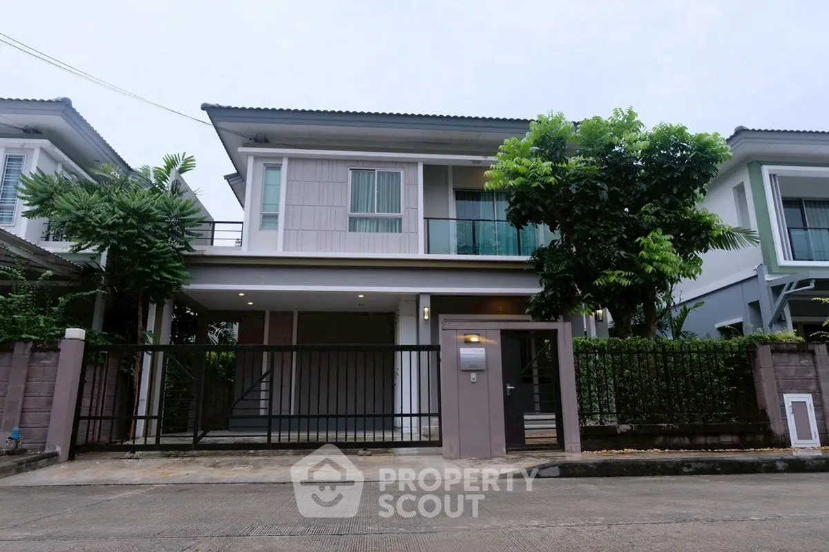 Modern two-story house with gated entrance and lush greenery
