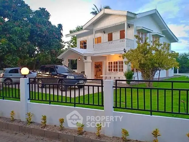 Charming two-story white house with lush garden and driveway, perfect family home.