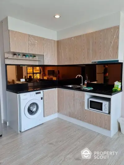 Sleek modern kitchen with integrated appliances, including a washing machine and built-in oven, complemented by stylish wood cabinetry and black countertops.