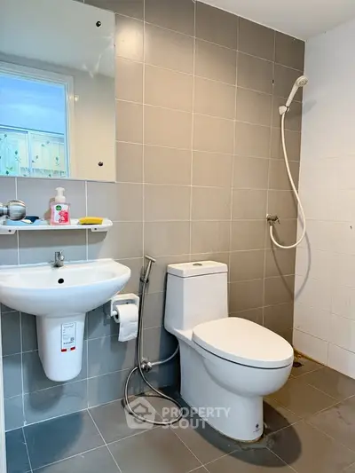 Modern bathroom with sleek fixtures and neutral tiles, featuring a shower and toilet.