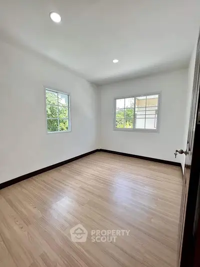 Spacious empty room with wooden flooring and large windows offering natural light.