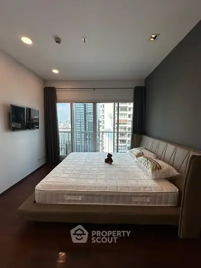 Modern bedroom with large windows and city view, featuring a stylish bed and wall-mounted TV.