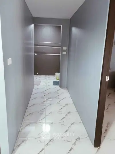 Modern hallway with marble flooring leading to a bathroom, showcasing sleek design and neutral tones.
