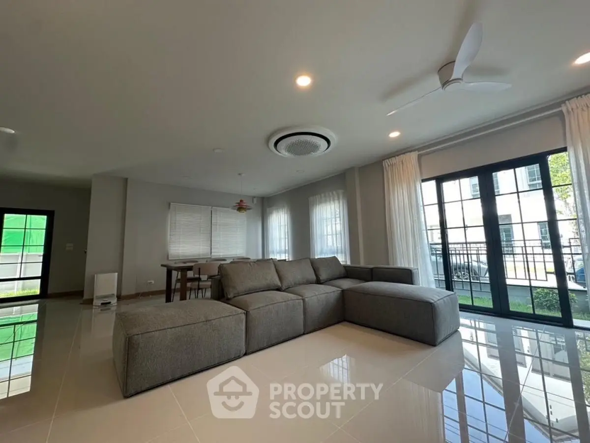 Spacious modern living room with large sofa and natural light from balcony.