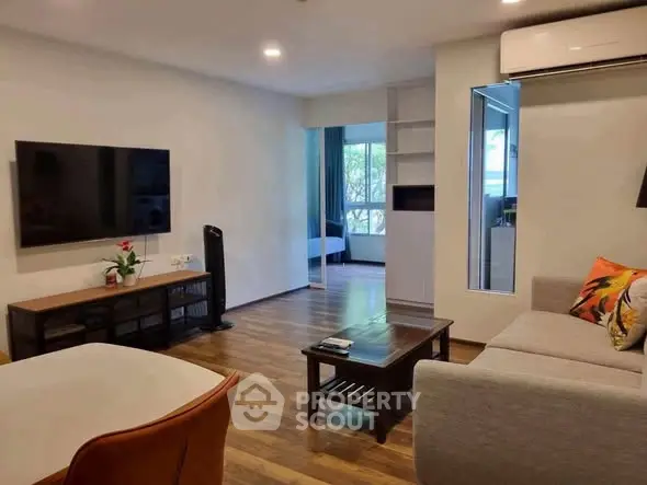 Modern living room with sleek furniture and large TV, open to a bright bedroom.