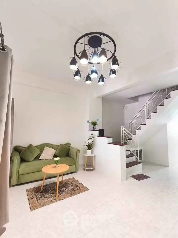 Modern living room with stylish lighting and staircase, featuring a cozy green sofa and elegant decor.