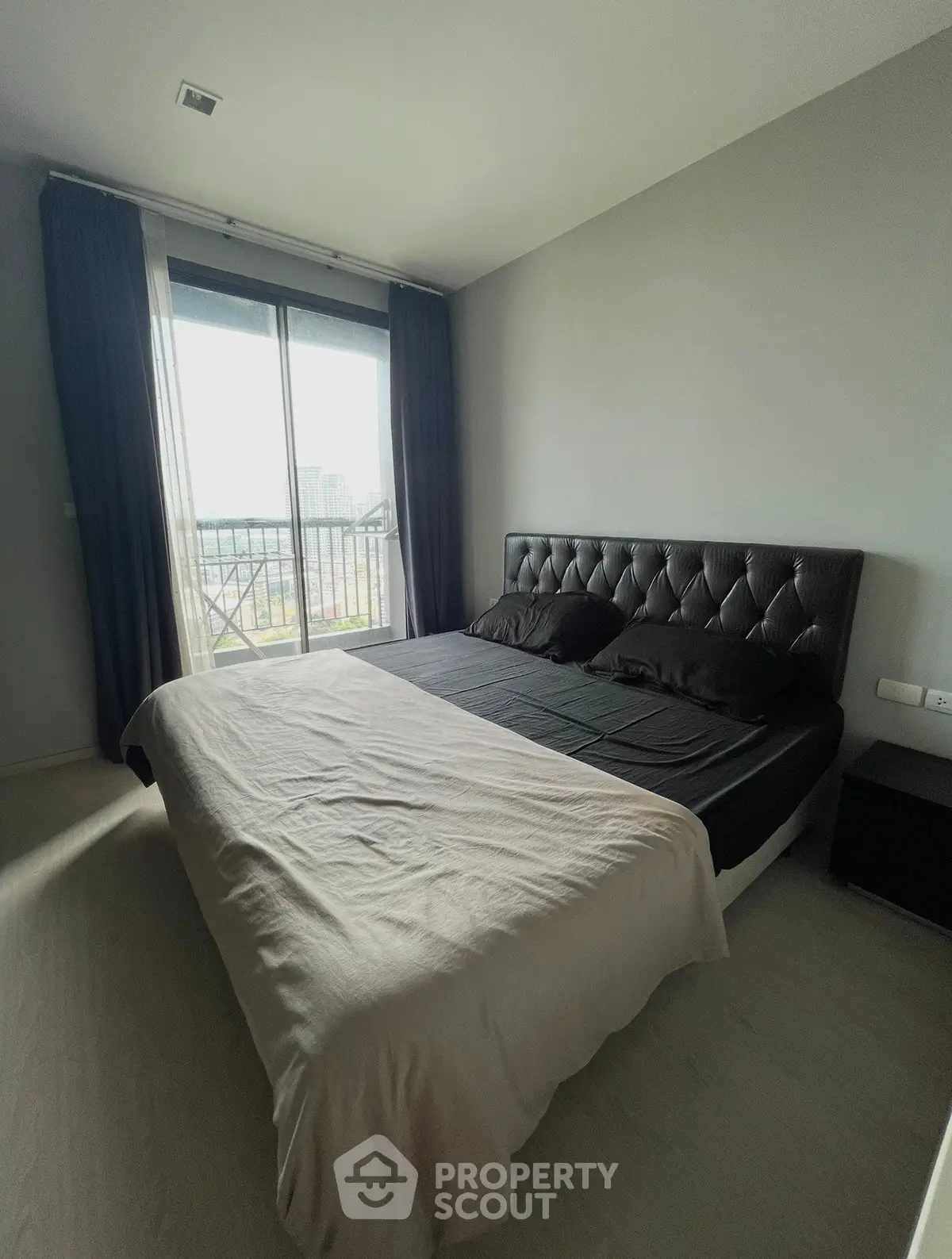 Spacious bedroom with large window and modern decor in a high-rise apartment.