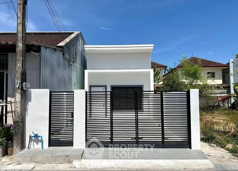 Modern minimalist house exterior with sleek black fence and clean white facade under clear blue sky.